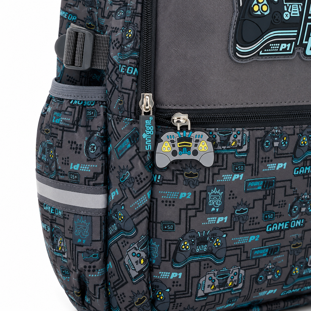 Close-up of a backpack featuring a dark gray and black video game theme print with blue and gray graphics, including game controllers, text like 'GAME ON!' and 'P1/P2', a gray game controller zipper pull, and a gray side pocket with reflective trim.