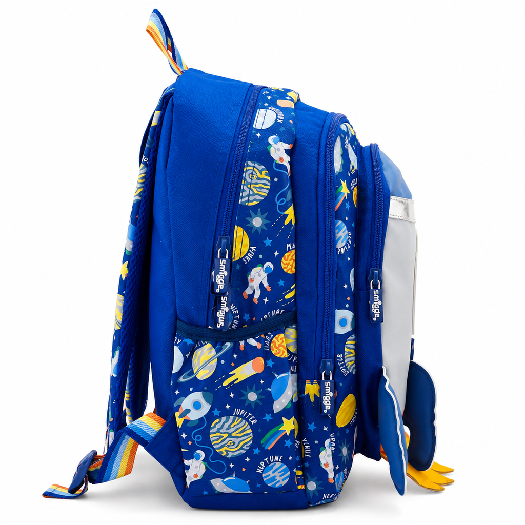 A blue school backpack with an outer space theme, featuring a pattern of planets, astronauts, rockets, and stars. The backpack has multiple zippered compartments, a front pocket, and a white side pocket with a blue penguin plush pull-out.