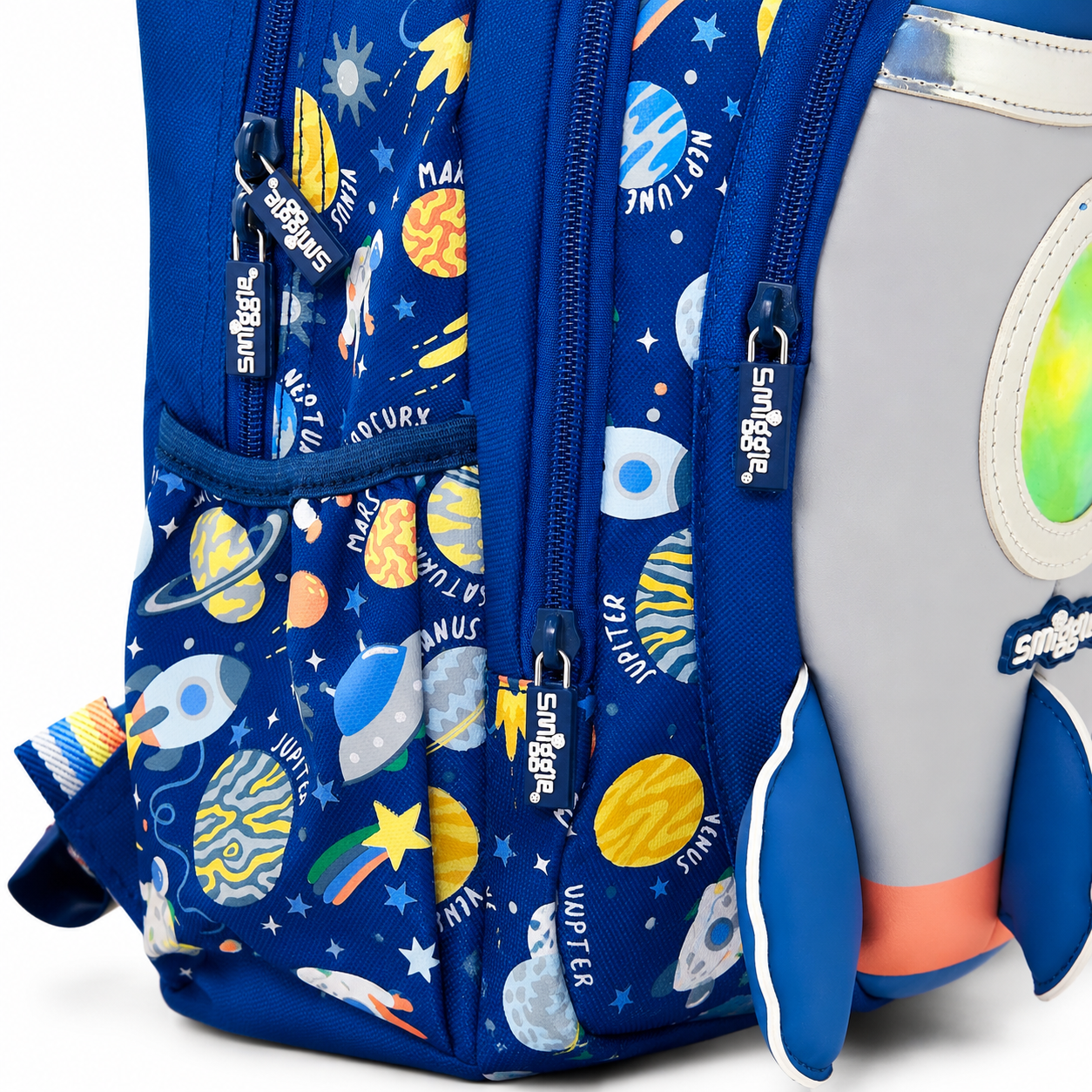 A close-up of a blue backpack with a colorful space-themed print featuring planets, stars, rockets, and zippers labeled 'Sungriz'. A gray rocket-shaped item is partially visible on the right side.